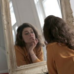 young-woman-looking-at-her-reflection-in-a-large-mirror.