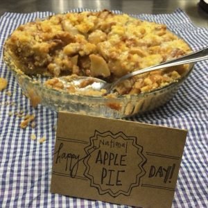 Homemade apple pie with a handwritten sign that says "Happy National Apple Pie Day!"