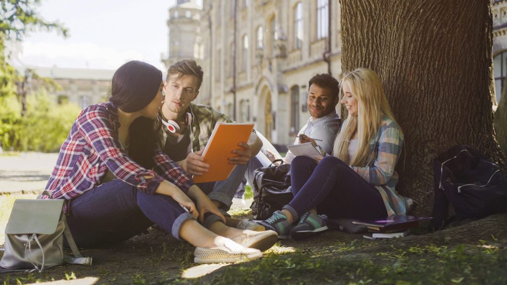 Four college students sitting outside, studying on campus.