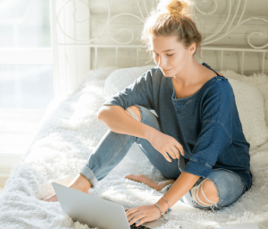 young woman sitting on her bed using a laptop