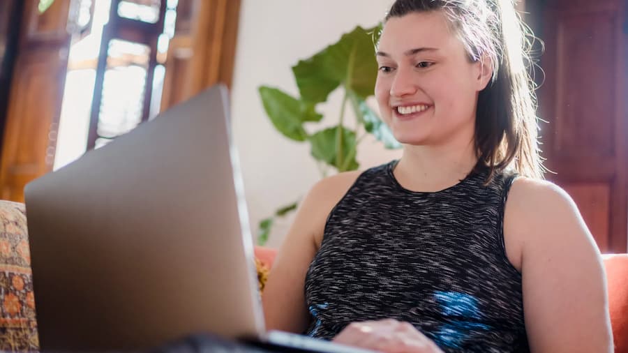 young woman in black tank top smiling while working on laptop