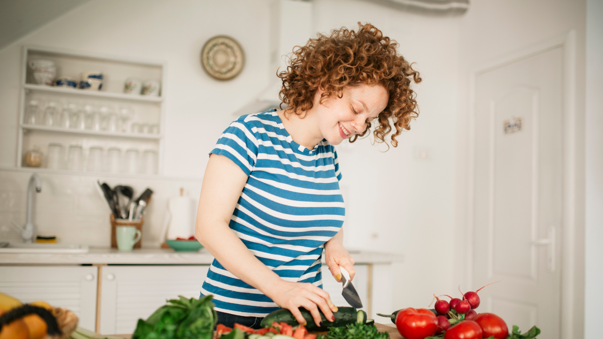curly haired woman in blue striped shirt cutting vegetables