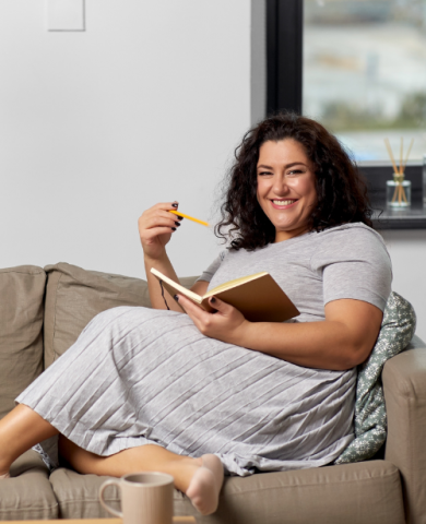 woman in gray dress sitting on a couch with a pencil and a journal
