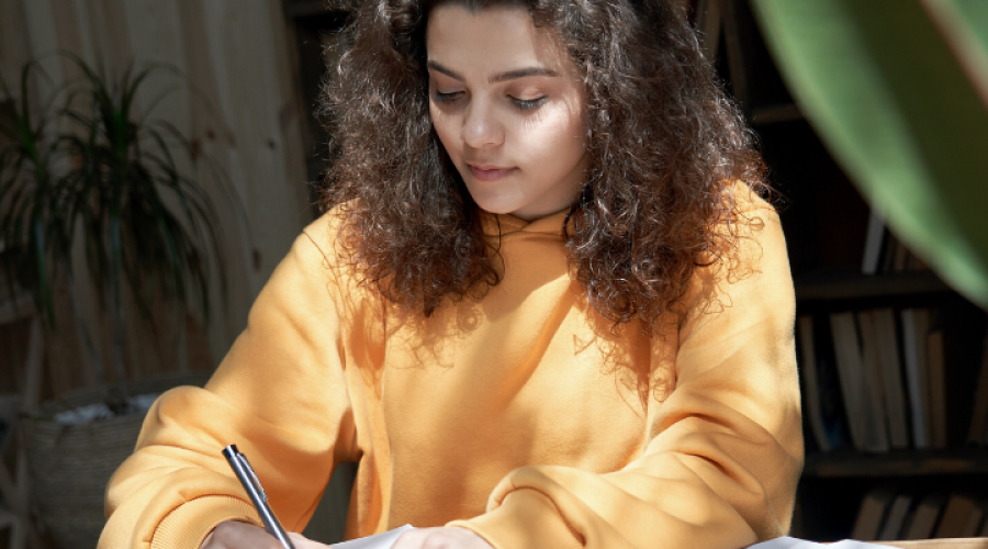 college-student-in-yellow-sweatshirt-focuses-on-coursework-1000--400-px